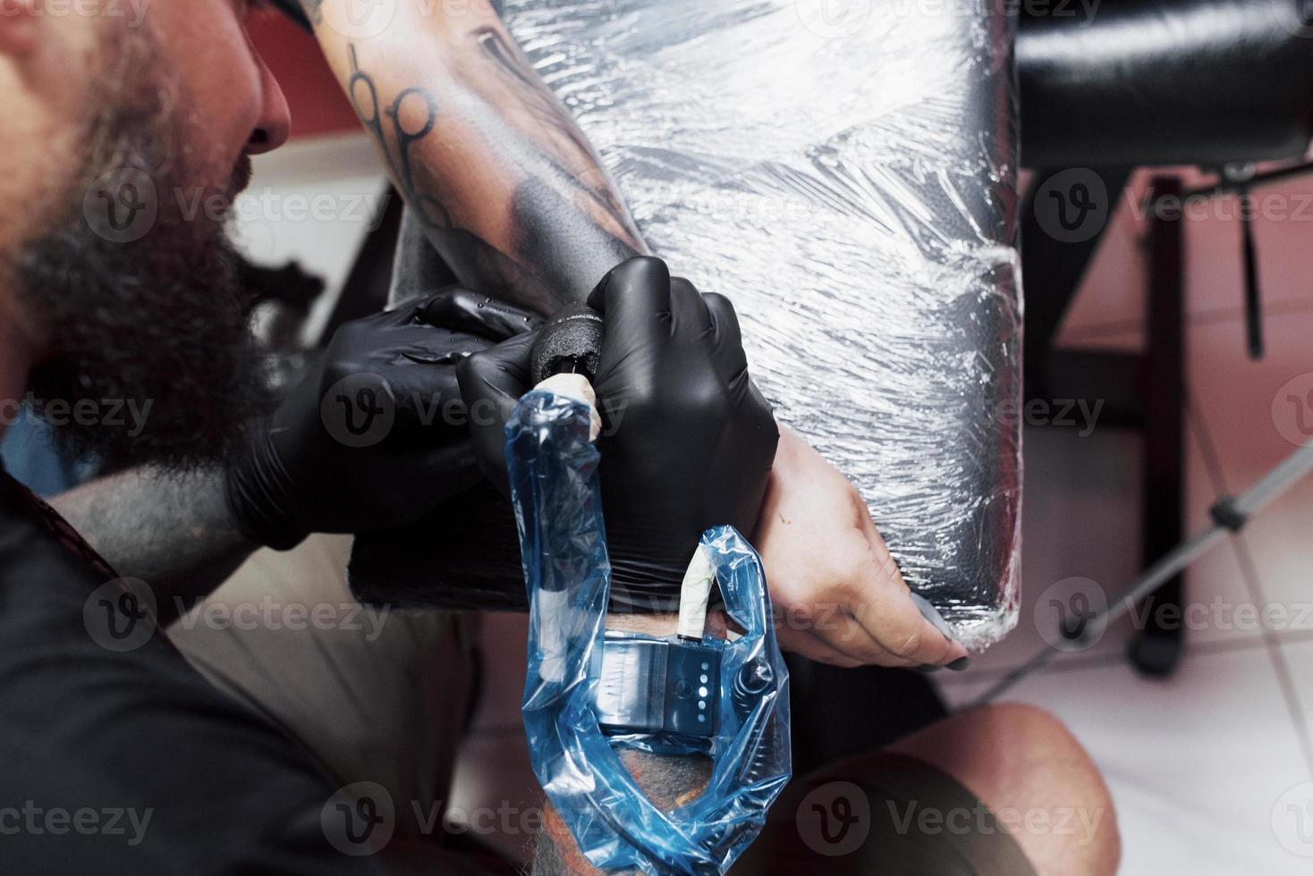 feche a máquina de tatuagem. mestre em luvas esterilizadas pretas criando uma imagem disponível com ele no salão foto