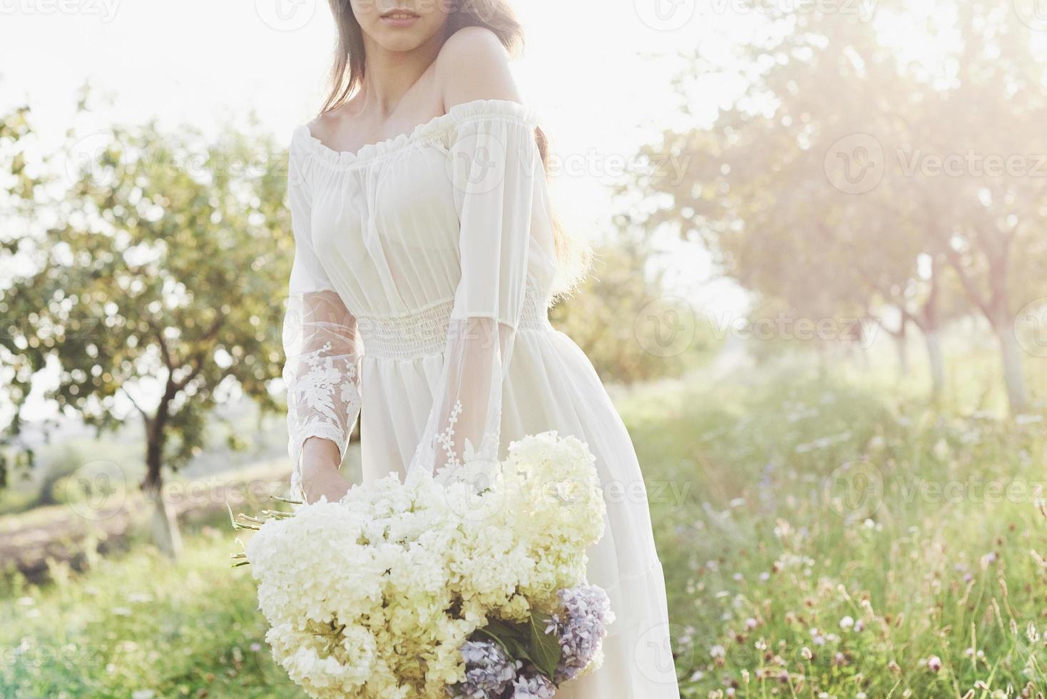 uma linda jovem em um vestido branco leve e um buquê de flores de verão faz um belo dia no jardim foto