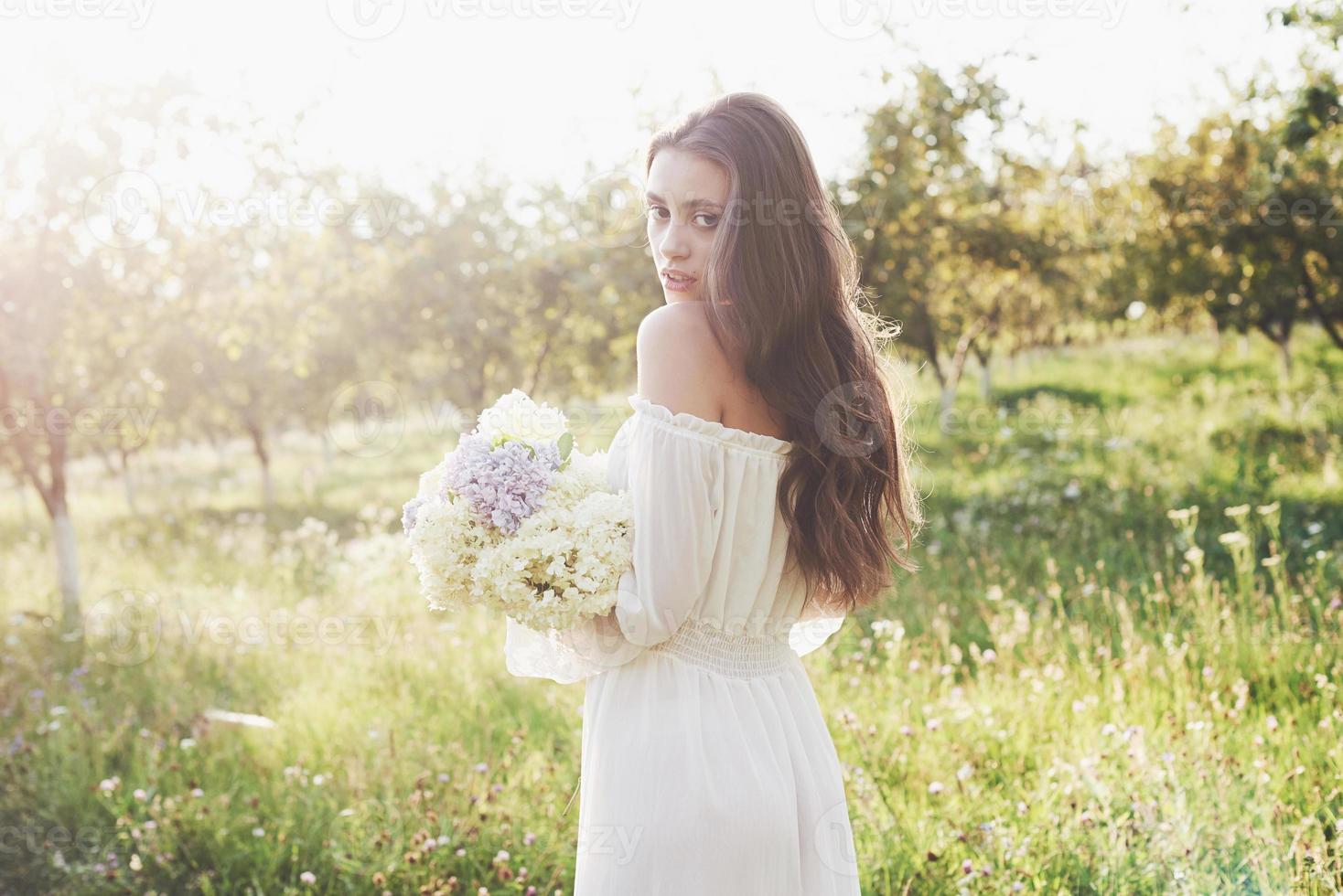 uma linda jovem em um vestido branco leve e um buquê de flores de verão faz um belo dia no jardim foto