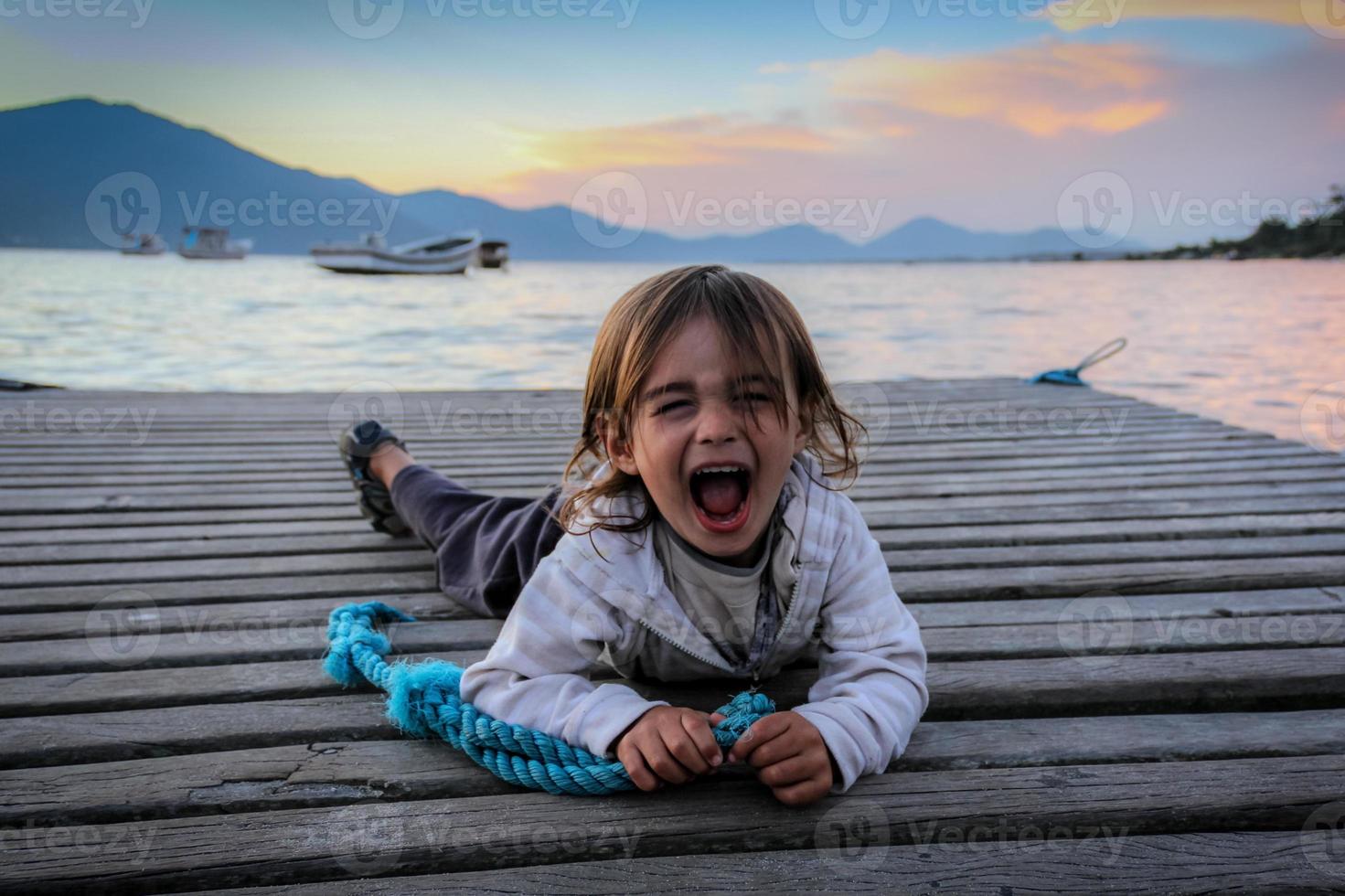 retrato de um menino gritando em diversão, deitado em uma doca. foto