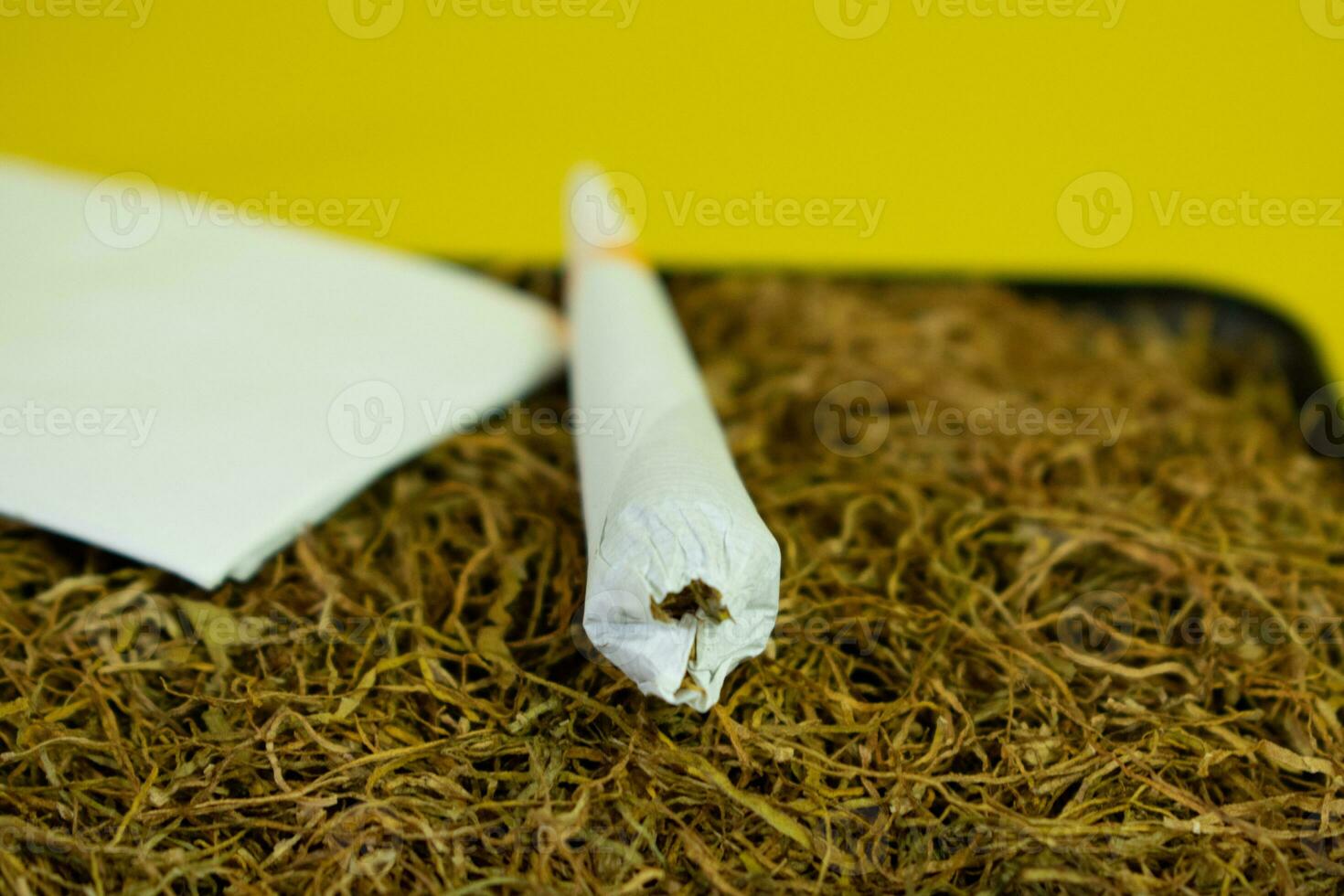 mão enrolado cigarro feito à mão e tabaco em amarelo fundo foto