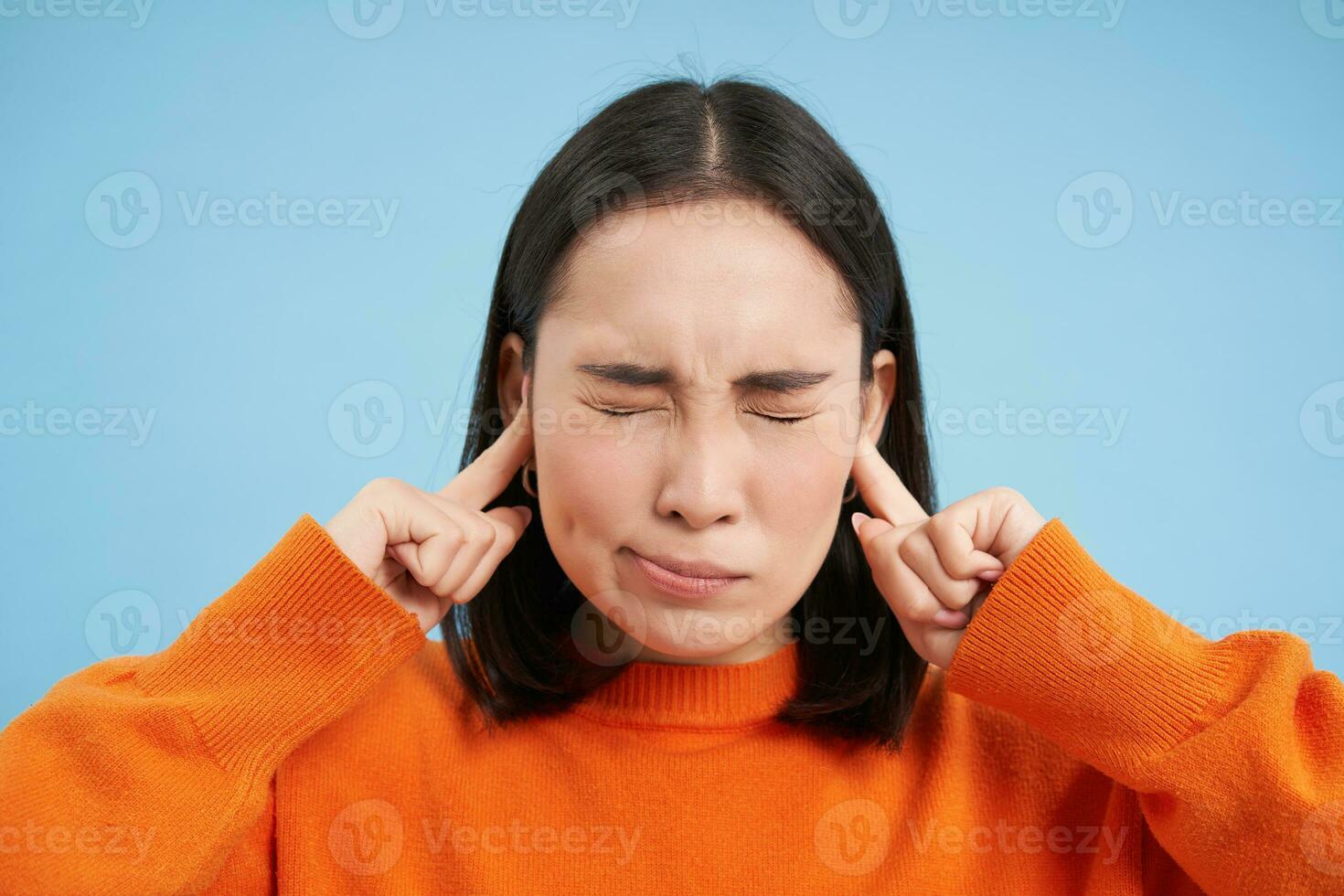 fechar acima do jovem mulher fecha dela orelhas com dedos e fecha olhos, irritado com alto barulho, irritante som, carrinhos sobre azul fundo foto