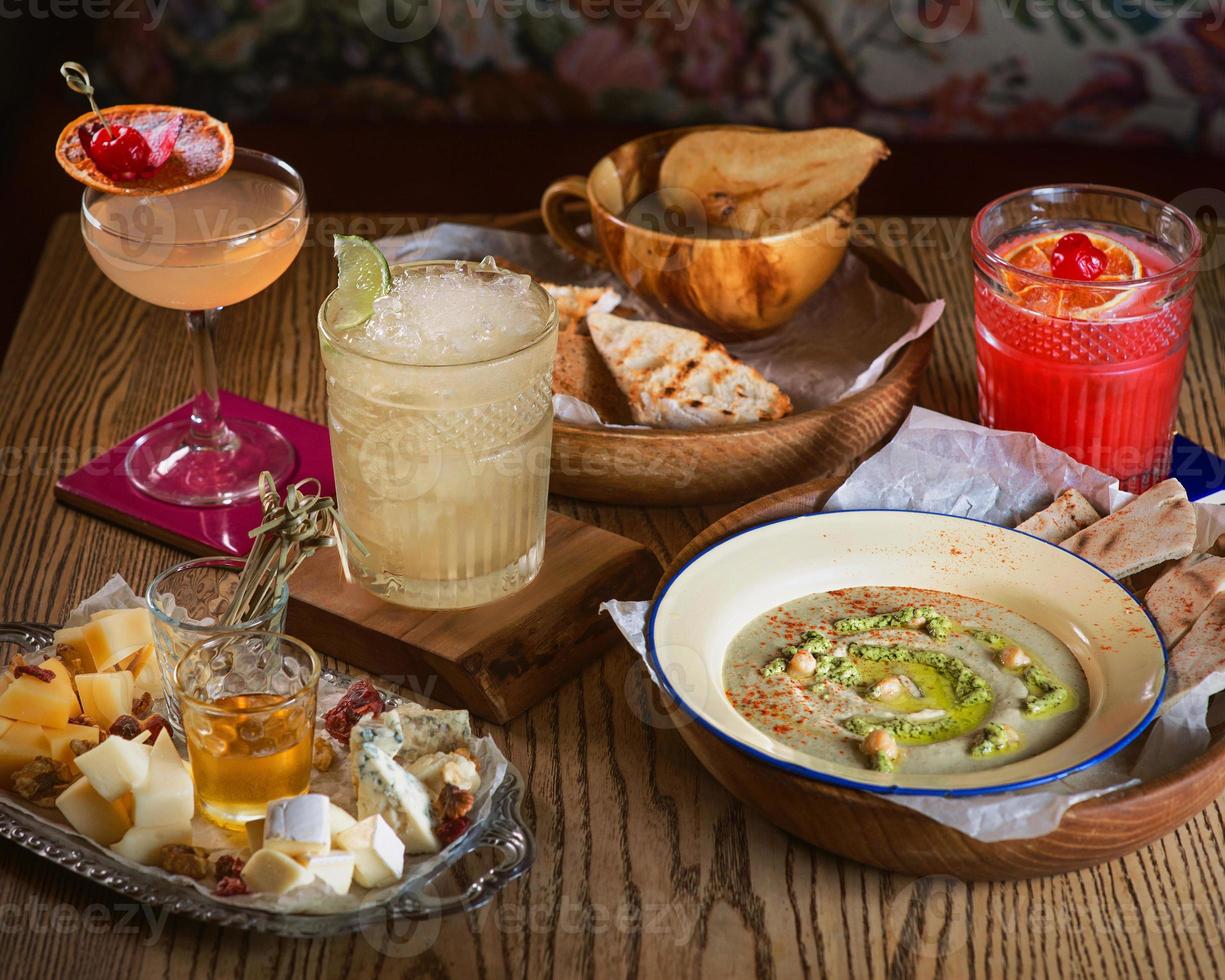 alimentos homus, geléia, diferentes tipos de queijo e coquetéis de álcool na mesa foto