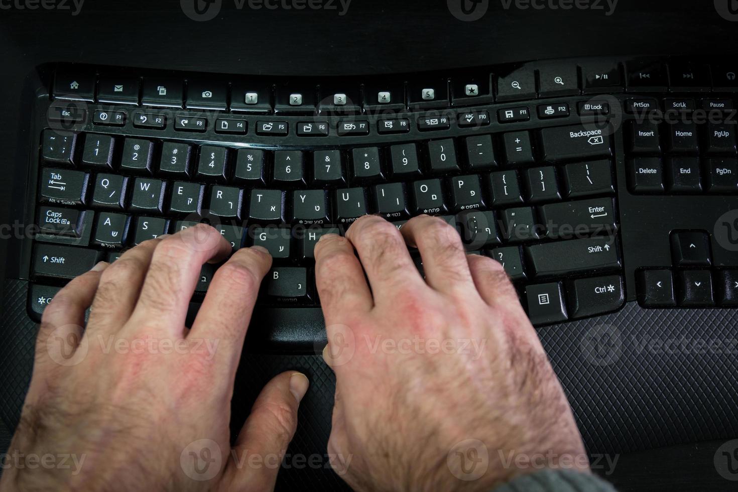 homem digitando em um teclado com letras em hebraico e inglês foto