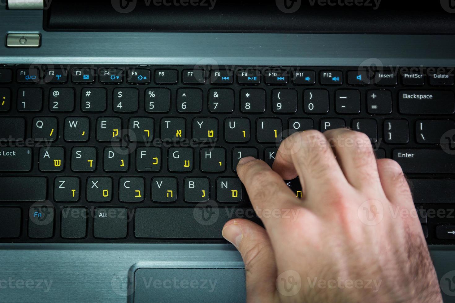 homem digitando em um teclado com letras em hebraico e inglês foto