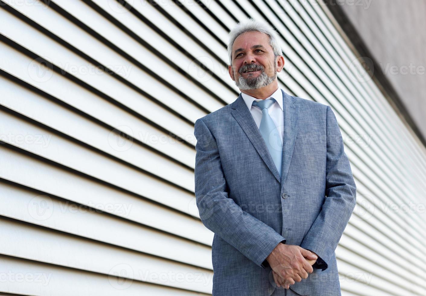 empresário sênior com os braços cruzados fora do prédio de escritórios moderno. foto