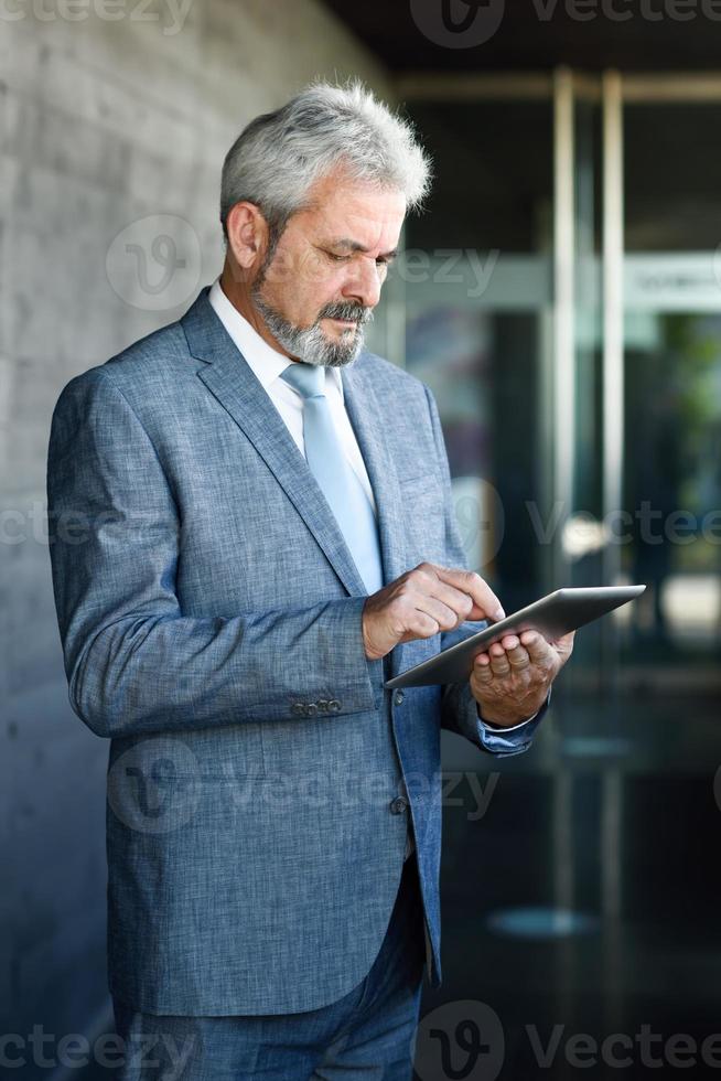 empresário sênior com computador tablet fora do prédio de escritórios moderno. foto