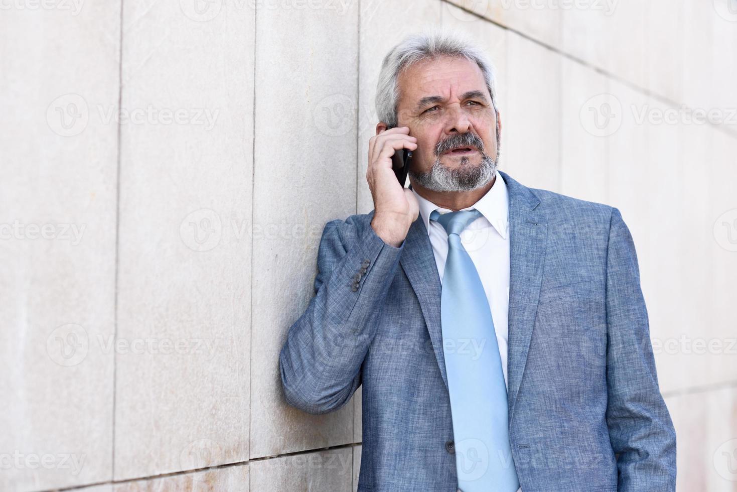 empresário sênior com smartphone fora do prédio de escritórios moderno. foto