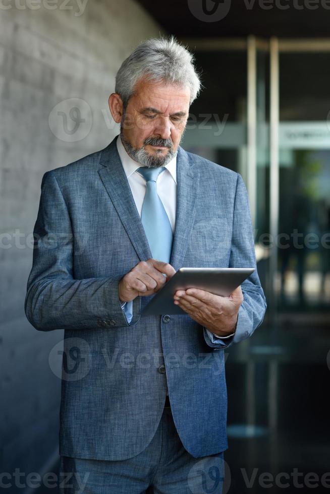 empresário sênior com computador tablet fora do prédio de escritórios moderno. foto