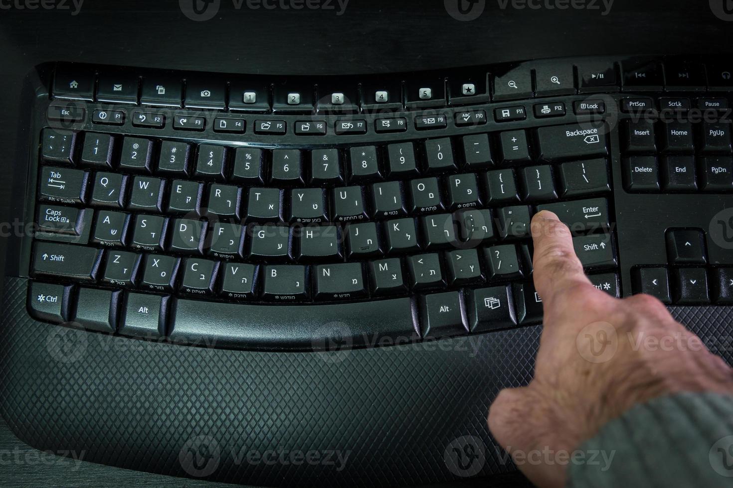 homem digitando em um teclado com letras em hebraico e inglês foto