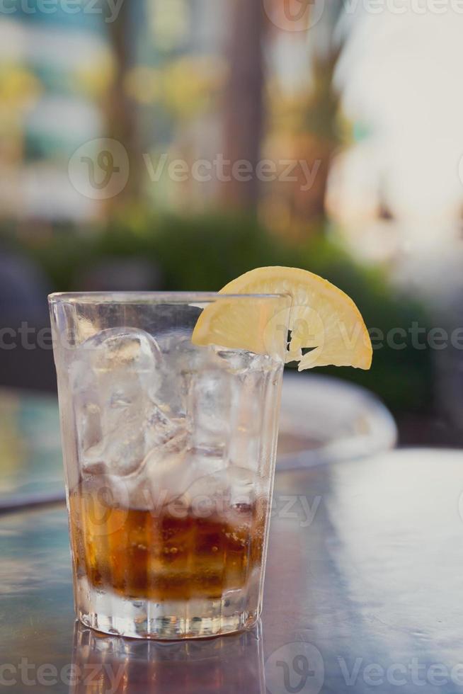 copo com coca-cola, gelo e limão em uma mesa do lado de fora foto