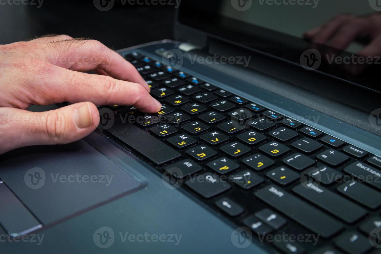 homem digitando em um teclado com letras em hebraico e inglês foto