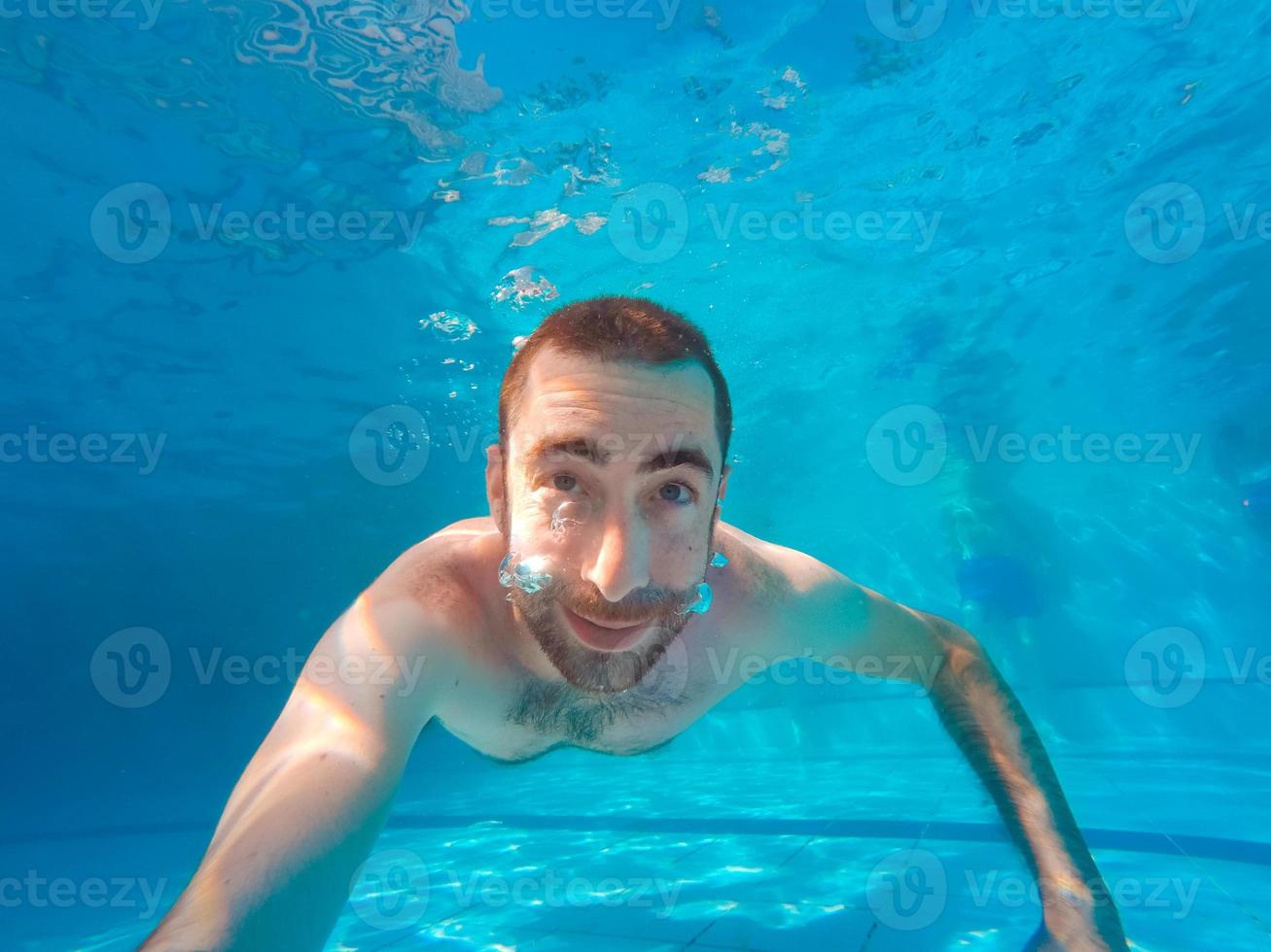 jovem bonito mergulhando debaixo d'água em uma piscina foto