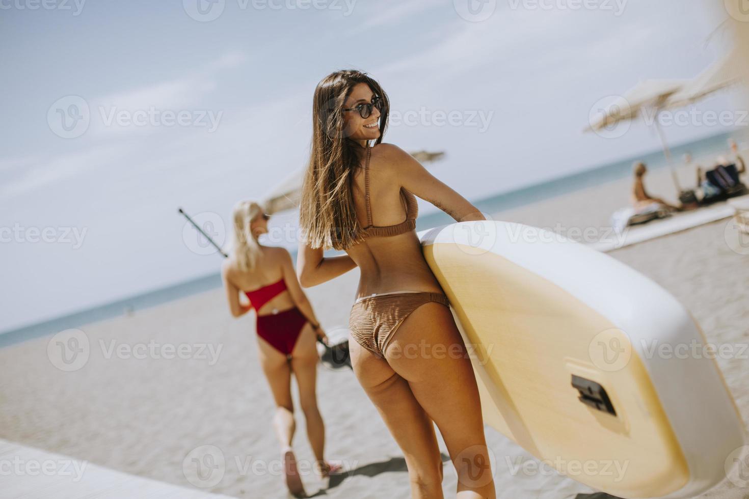 duas mulheres jovens com prancha de remo na praia em um dia de verão foto
