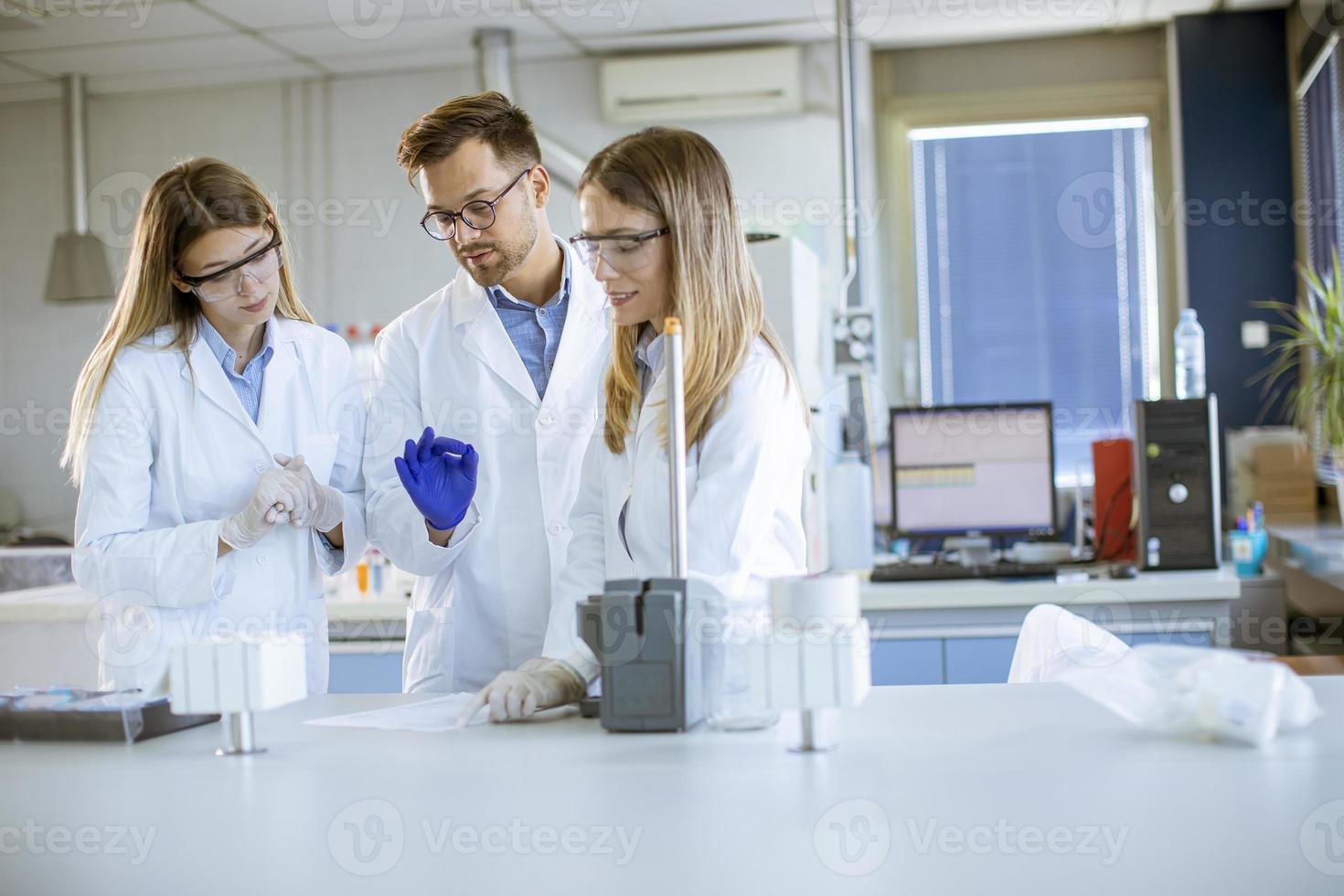 pesquisadores em roupas de trabalho de proteção em pé no laboratório e analisando amostras de líquidos em equipamentos de cromatografia de íons foto