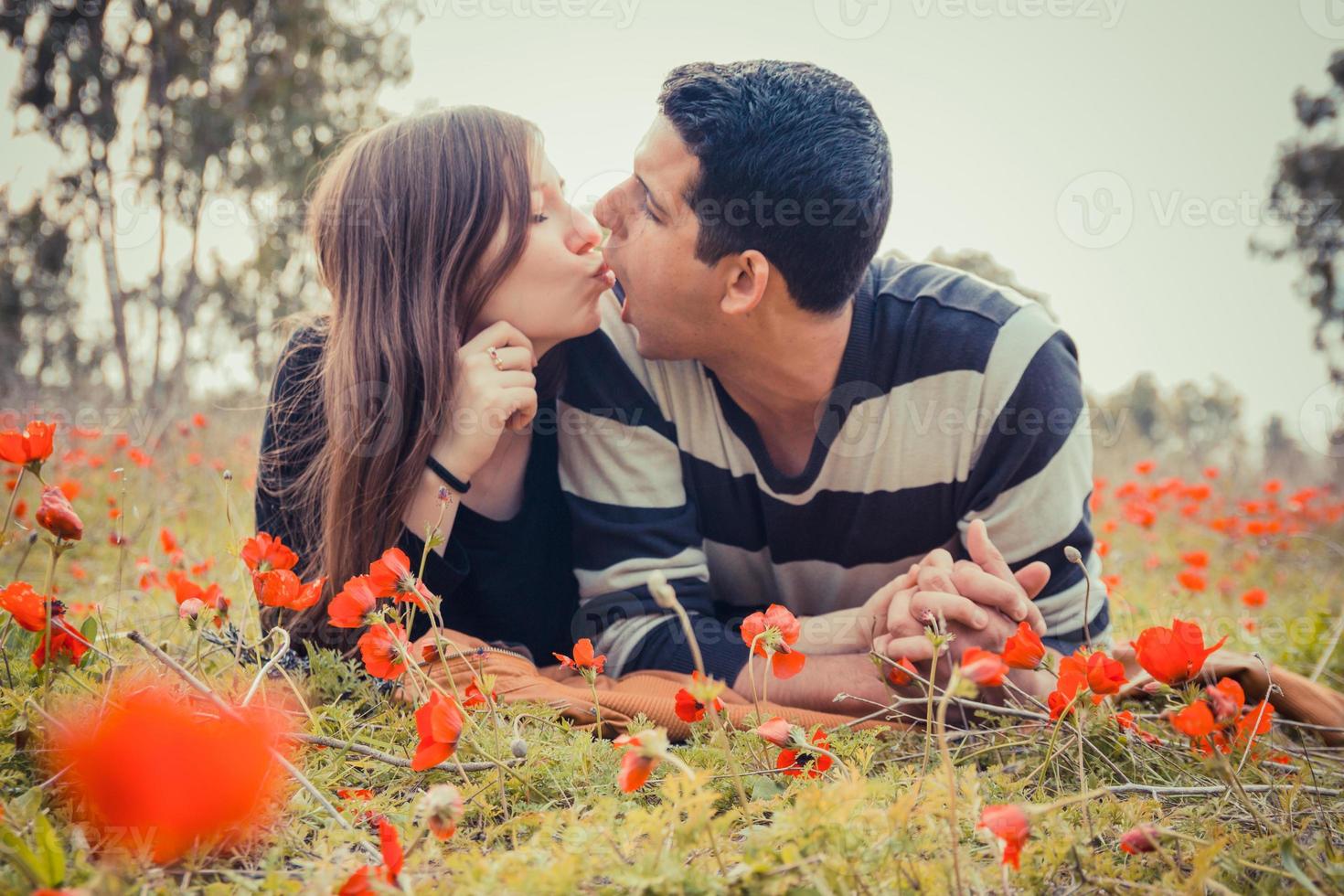 jovem casal fazendo caretas um para o outro enquanto se deitava na grama em um campo de papoulas vermelhas foto