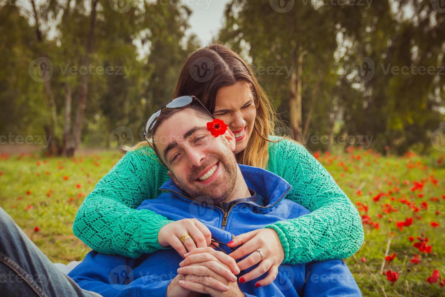 jovem casal sentado na grama em um campo de papoulas vermelhas, sorrindo e rindo um do outro foto