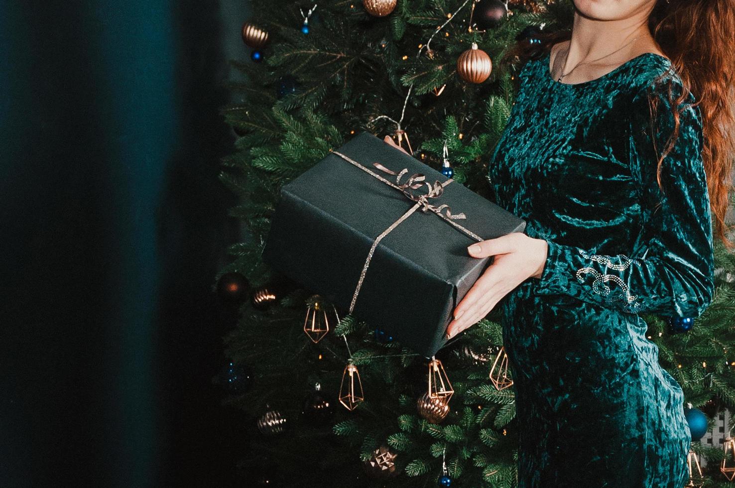 mulher com uma caixa de presente perto da árvore de natal foto