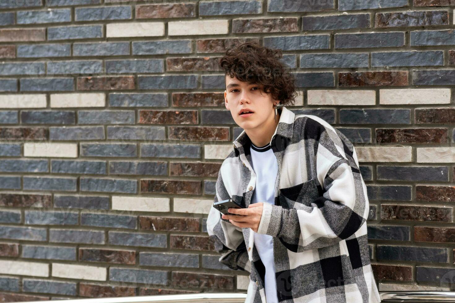 jovem homem com uma telefone contra uma tijolo parede foto