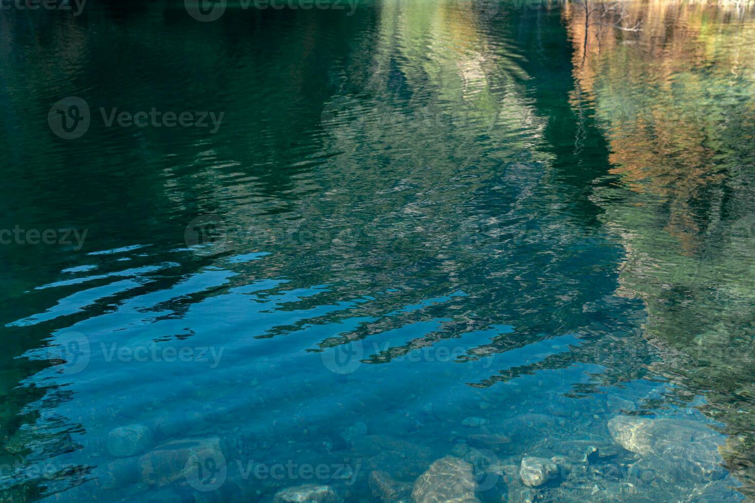 ondulado água superfície do uma Claro floresta lago com reflexão do montanhas e céu foto