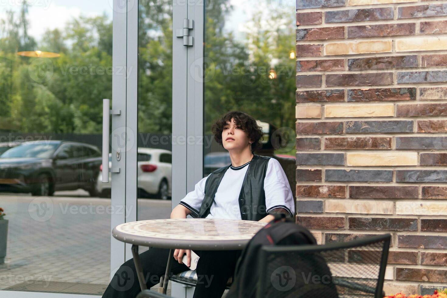 jovem homem esperando para alguém sentado às a ao ar livre cantina mesa foto