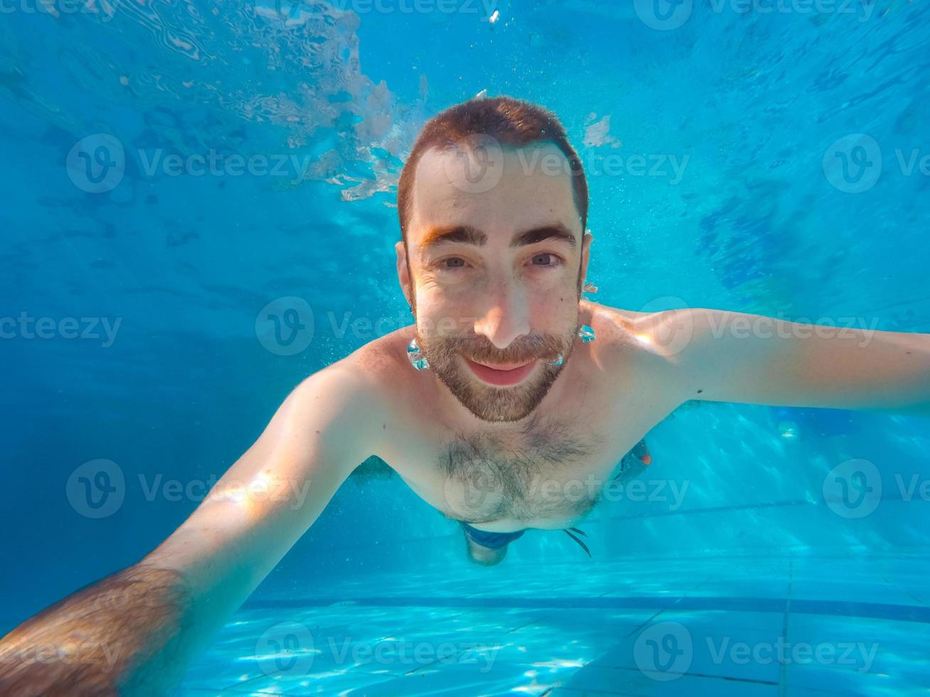 jovem bonito mergulhando debaixo d'água em uma piscina foto