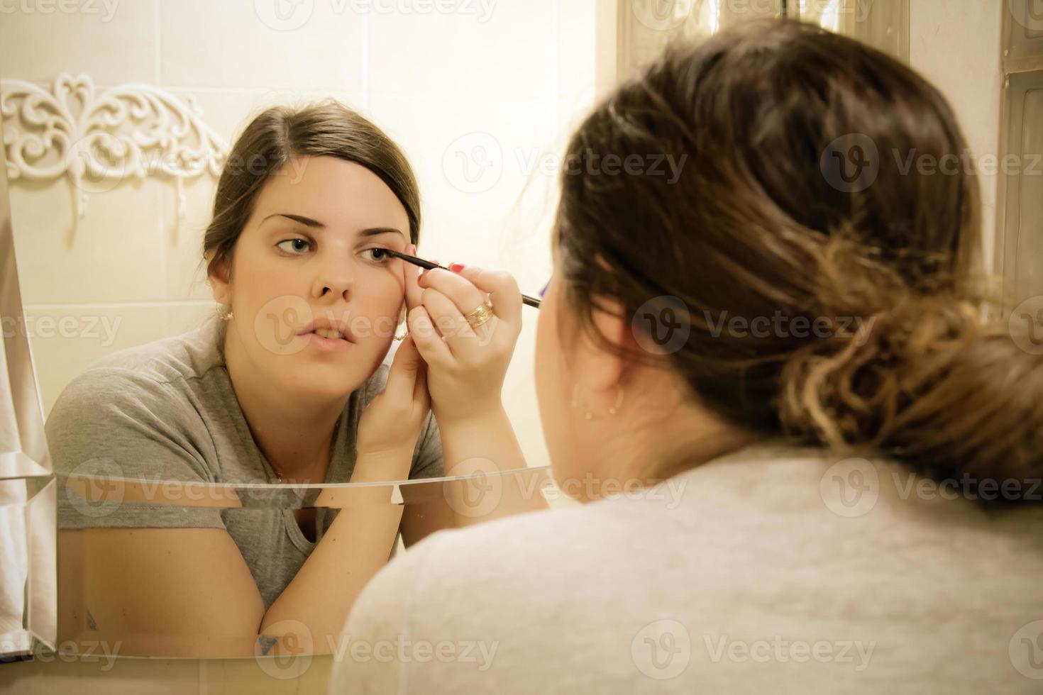 mulher colocando delineador na frente de um espelho foto