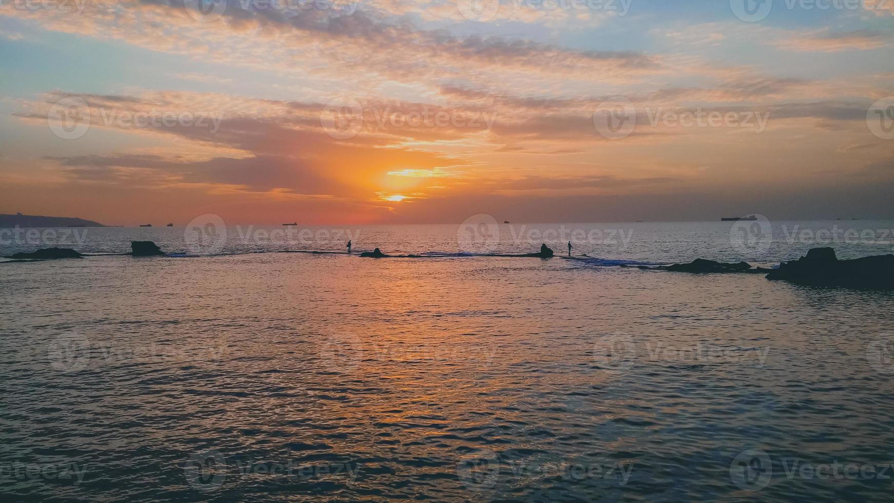 bela vista do pôr do sol sobre o mar com a silhueta de navios e pescadores foto