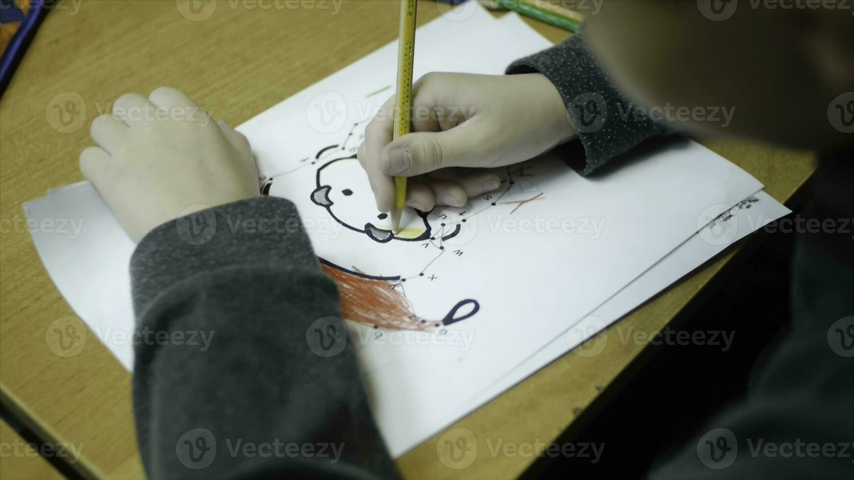 Alto ângulo Visão do Garoto desenhando com cor lápis em papel às escrivaninha dentro sala de aula. grampo. uma fofa pequeno Garoto desenhando com uma lápis fechar acima foto