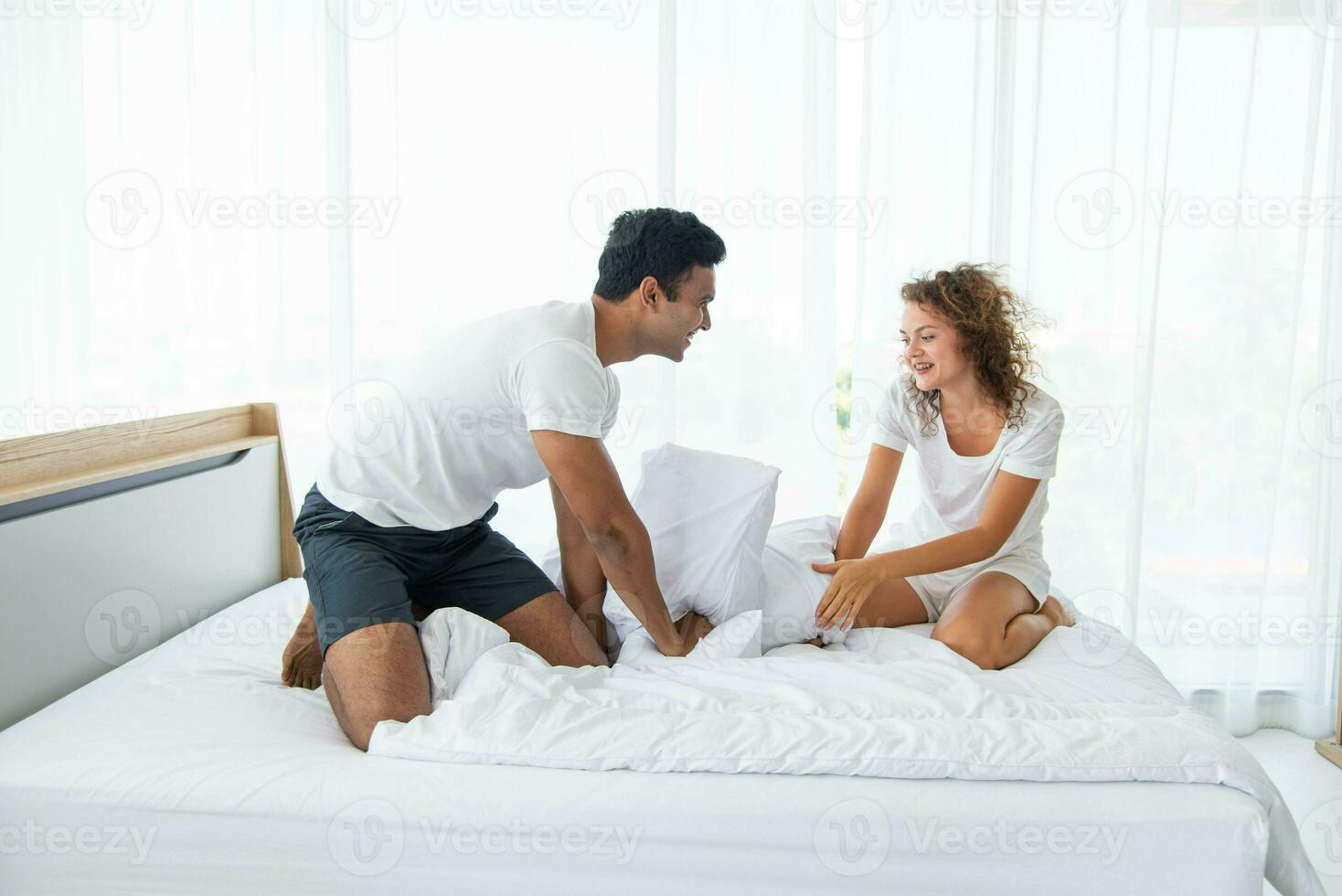 lindo casal tendo Diversão de brigando com uma travesseiro em cama depois de acordando acima dentro brilhante quarto. foto