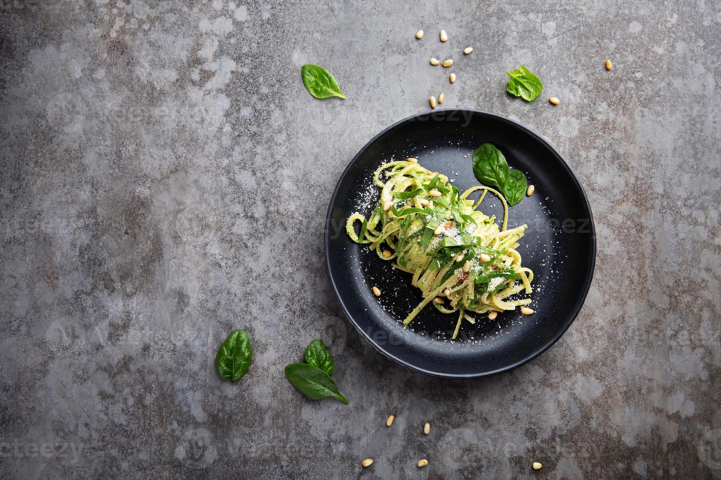 espaguete com espinafre, pinhão e queijo parmesão em um prato sobre uma mesa cinza foto