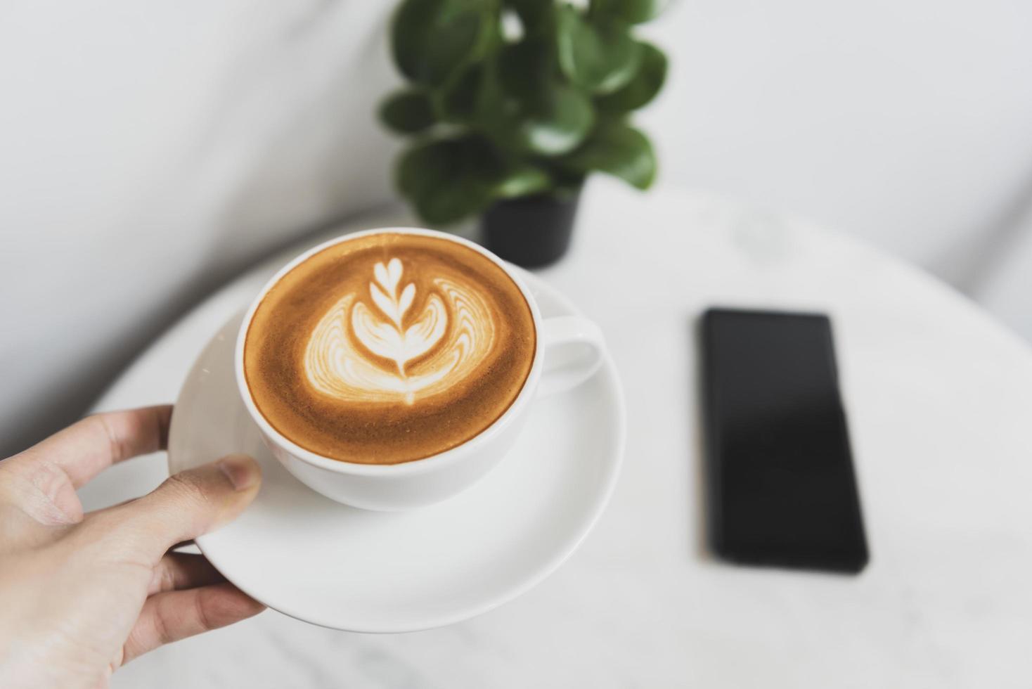 mão segurando o café com leite ou cappuccino com espuma espumosa, vista superior da xícara de café no café. foto