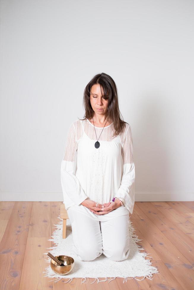 mulher bonita durante uma sessão de meditação. vestido com roupas brancas, sala vazia com piso de madeira. fundo branco foto