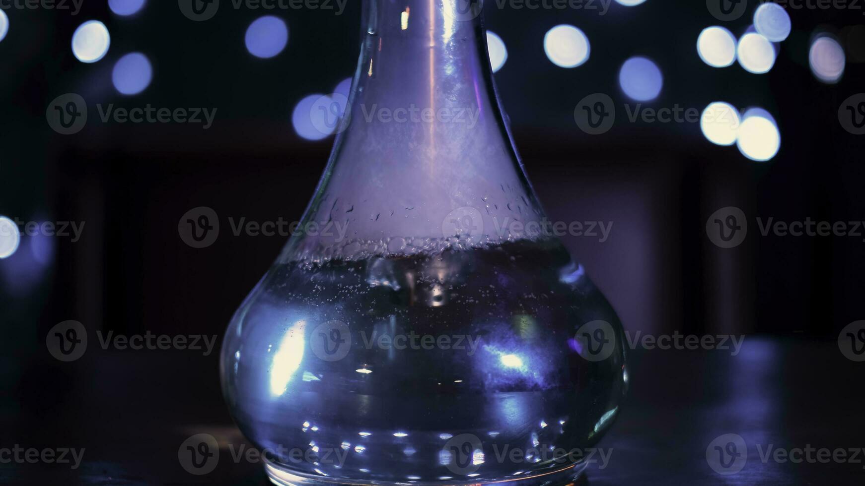 fumar narguilé em Sombrio mesa em azul luzes fundo. meios de comunicação. vidro narguilé frasco com transparente líquido dentro a Sombrio quarto do uma Barra ou restaurante. foto