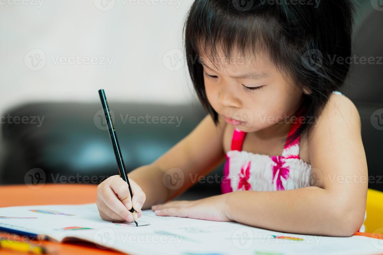 criança fofa asiática segurando giz de cera preto para colorir no livro. garota séria com lição de casa. foto