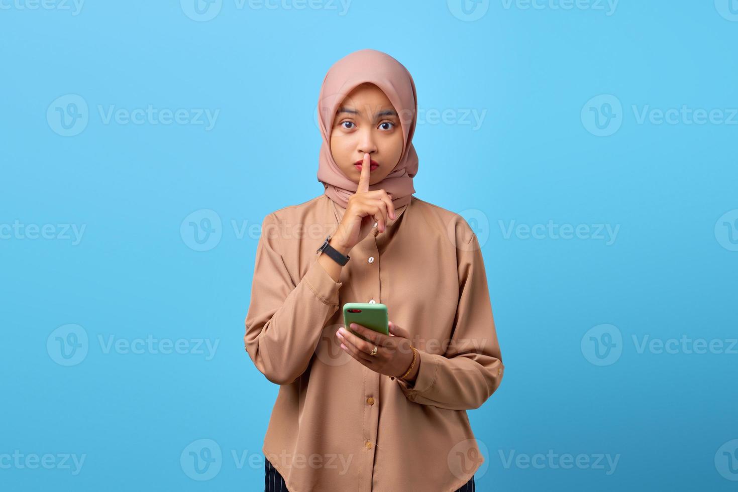 retrato de uma jovem mulher asiática segurando um telefone celular e fazendo gesto de silêncio com os dedos foto