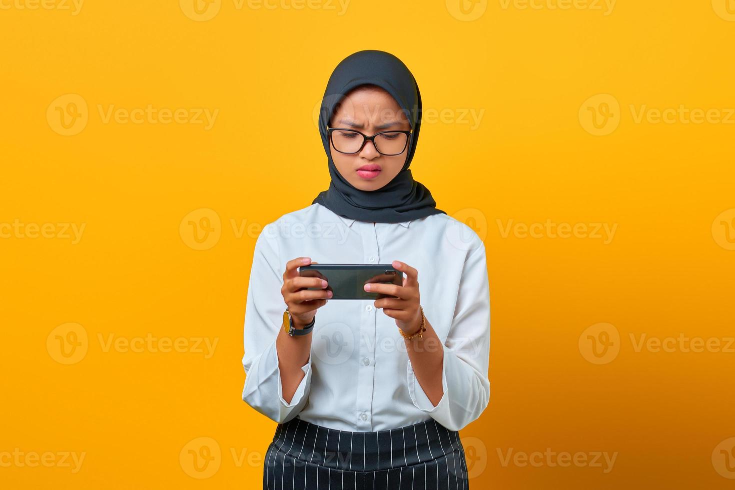 jovem e atraente mulher asiática usando o celular, jogando no fundo amarelo foto