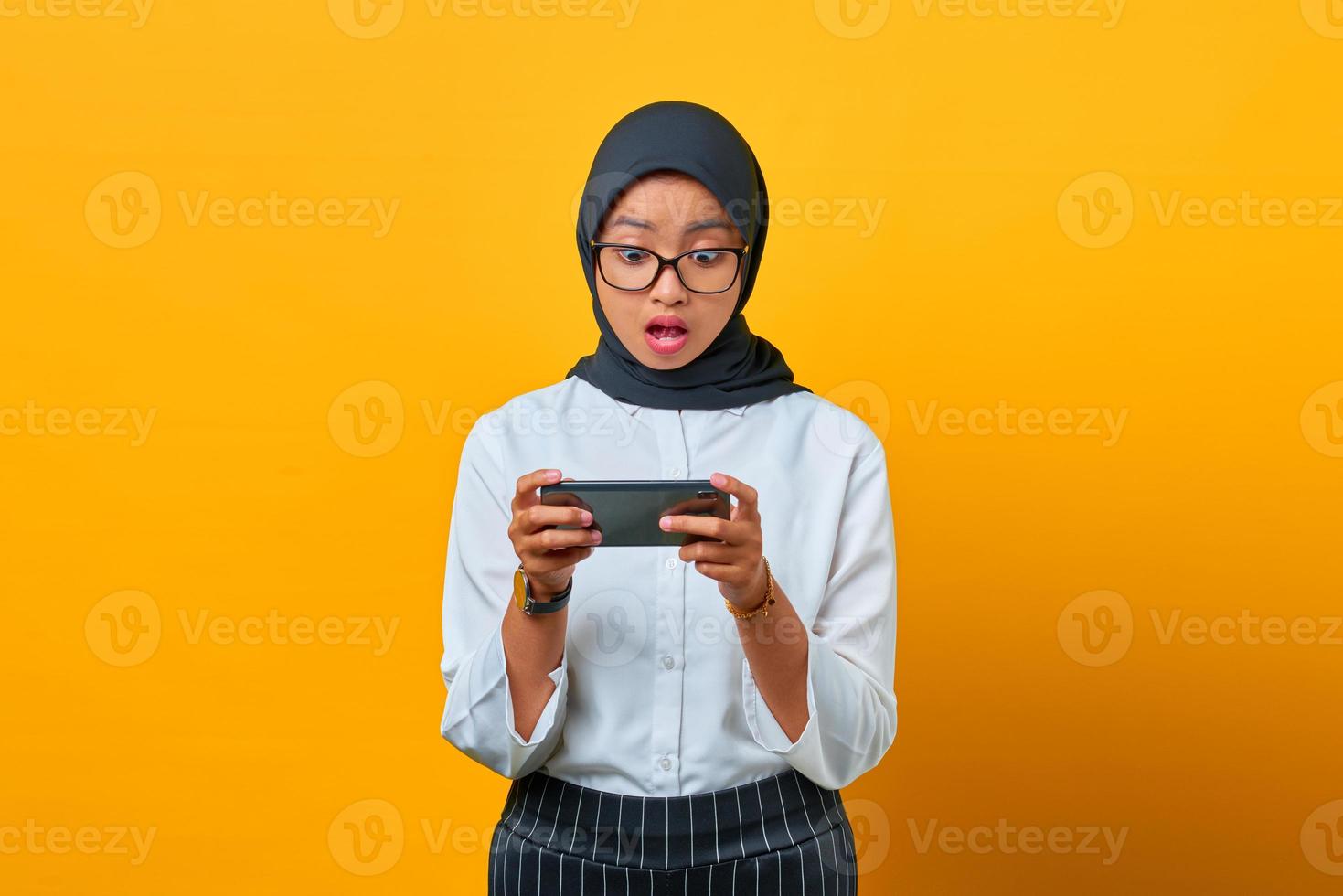 Surpreendeu a jovem mulher asiática usando o celular para jogar no fundo amarelo foto