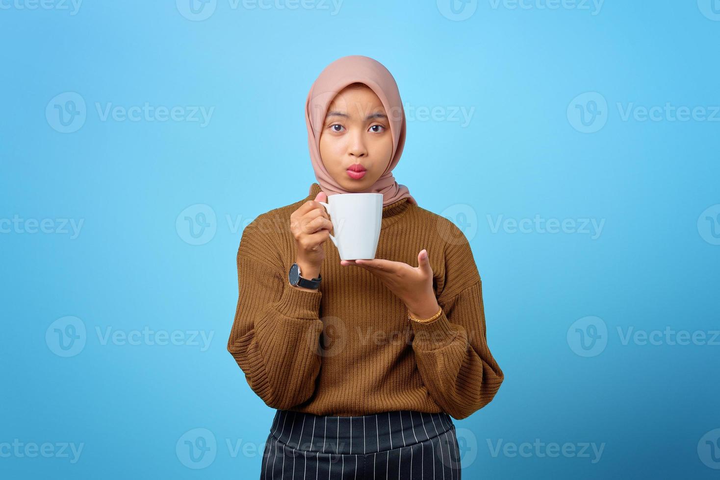 bela jovem asiática segurando uma caneca e bebendo chá no fundo azul foto