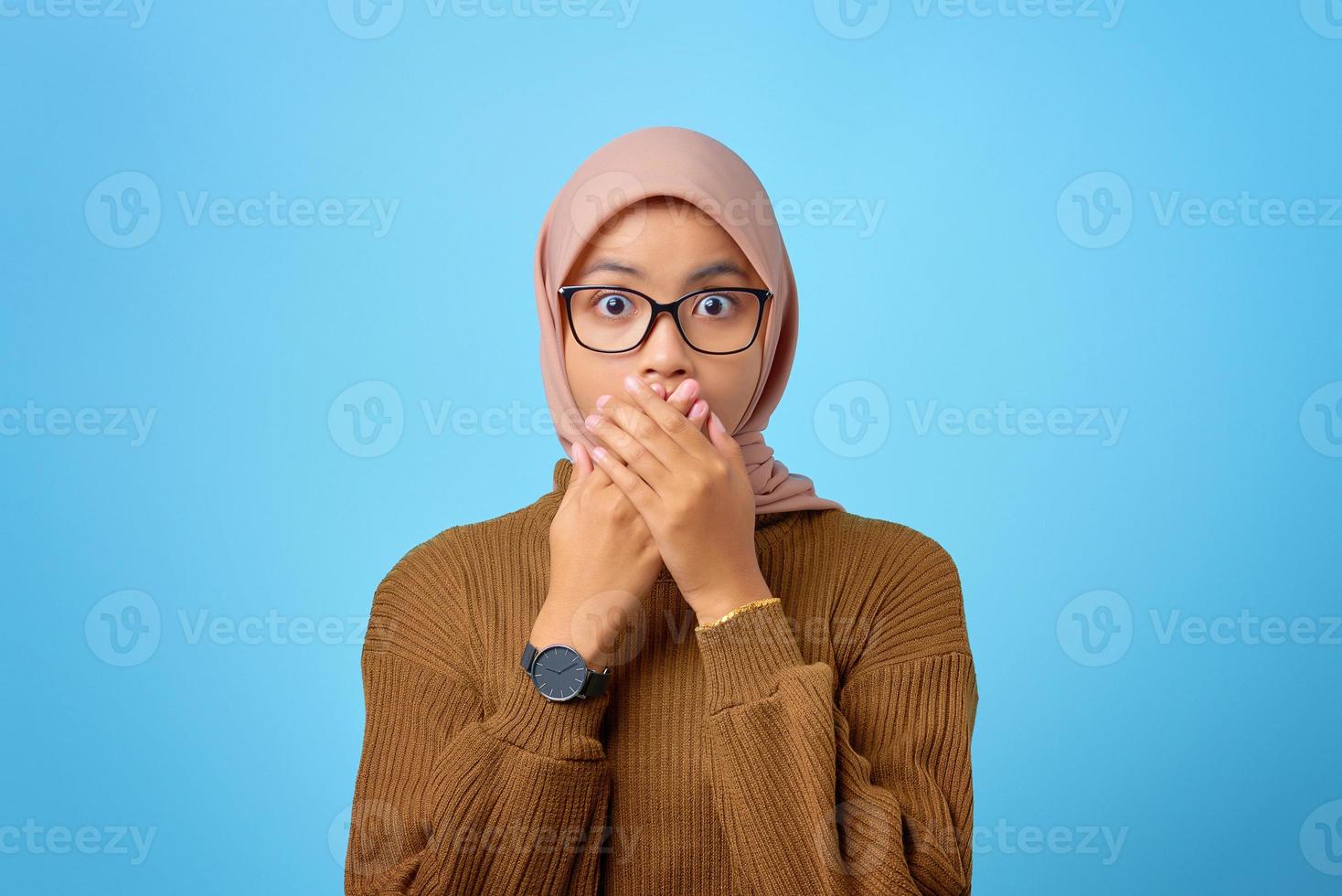 surpresa jovem asiática cobrindo a boca com a mão sobre fundo azul foto