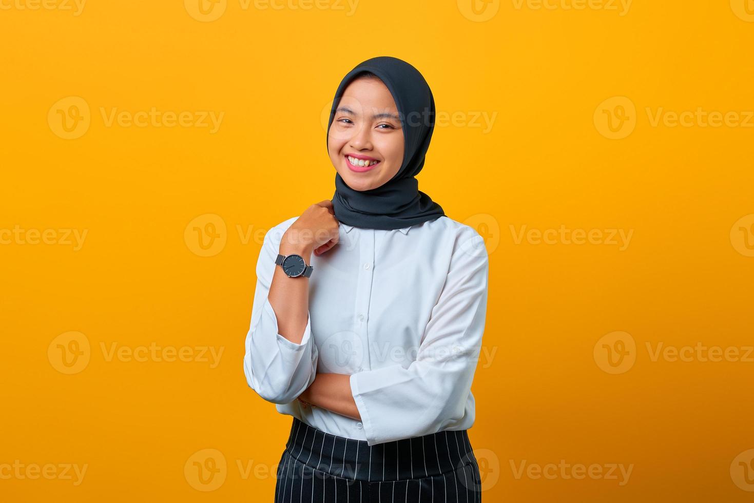 mulher asiática jovem e alegre erguida a mão com o braço cruzado isolado sobre um fundo amarelo foto