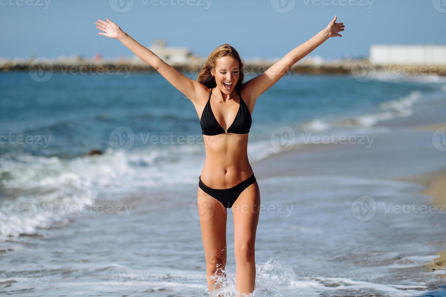jovem loira com corpo bonito em trajes de banho em uma praia tropical com os braços abertos. foto