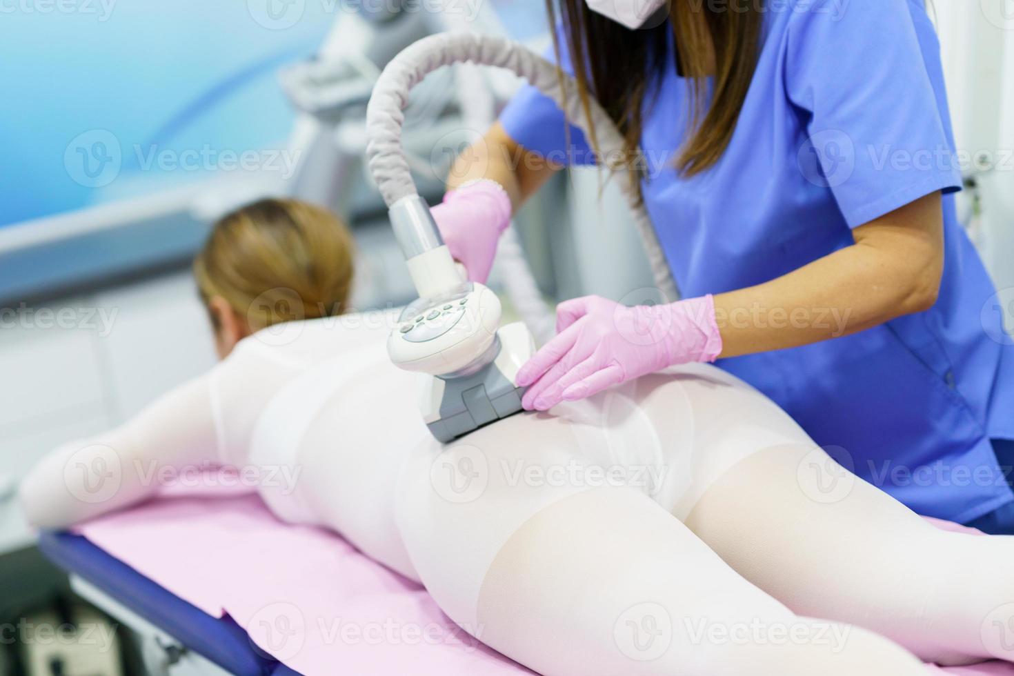 mulher em um terno branco especial fazendo massagem anticelulite com aparelho de spa foto