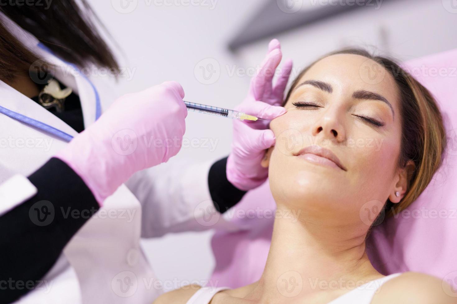 médico injetando ácido hialurônico nas maçãs do rosto de uma mulher como tratamento de rejuvenescimento facial. foto