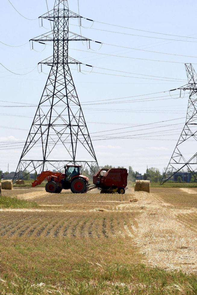 trator e enfardadeira vermelhos trabalhando sob torres hidrelétricas foto