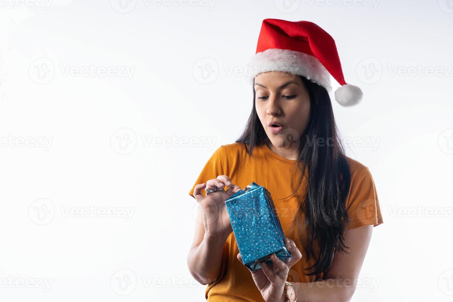 jovem latina com um chapéu de Papai Noel, abrindo uma caixa de presente de Natal. fundo branco foto