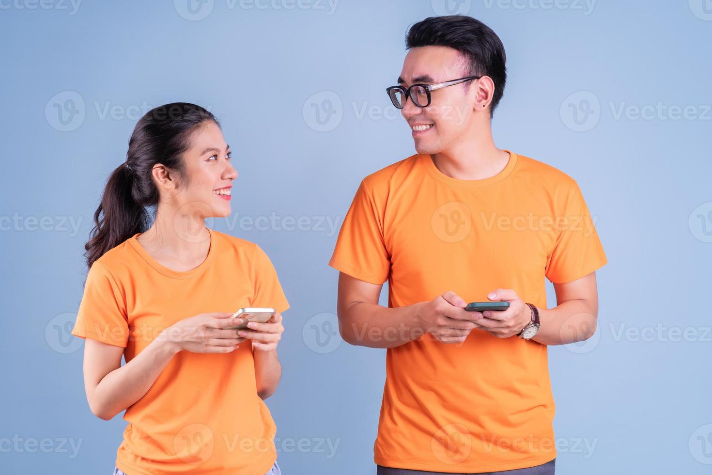 jovem casal asiático vestindo camiseta laranja sobre fundo azul foto