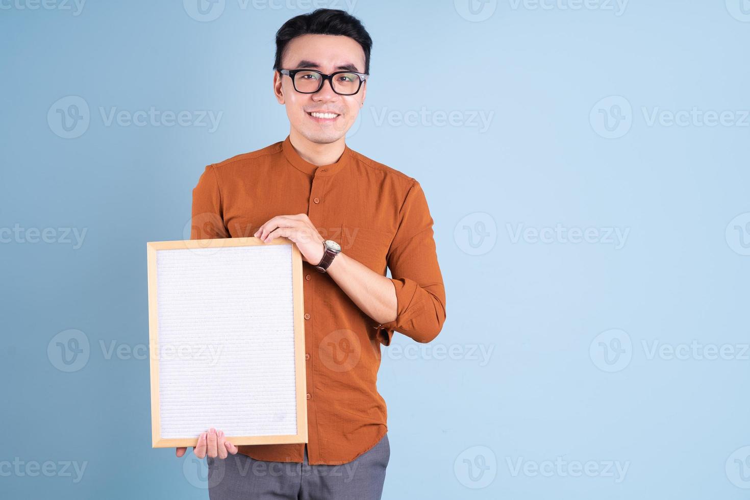 jovem asiático segurando um quadro branco sobre fundo azul foto
