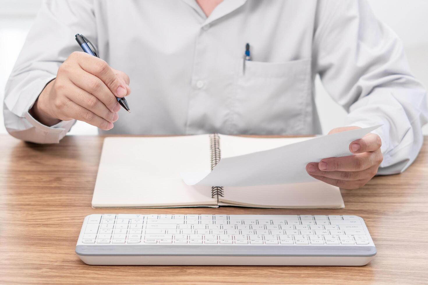 uma homem escrever em a papel Verifica serviço Lista dentro escritório com reparar parte do carro e computador portátil computador caderno teclado em madeira mesa foto