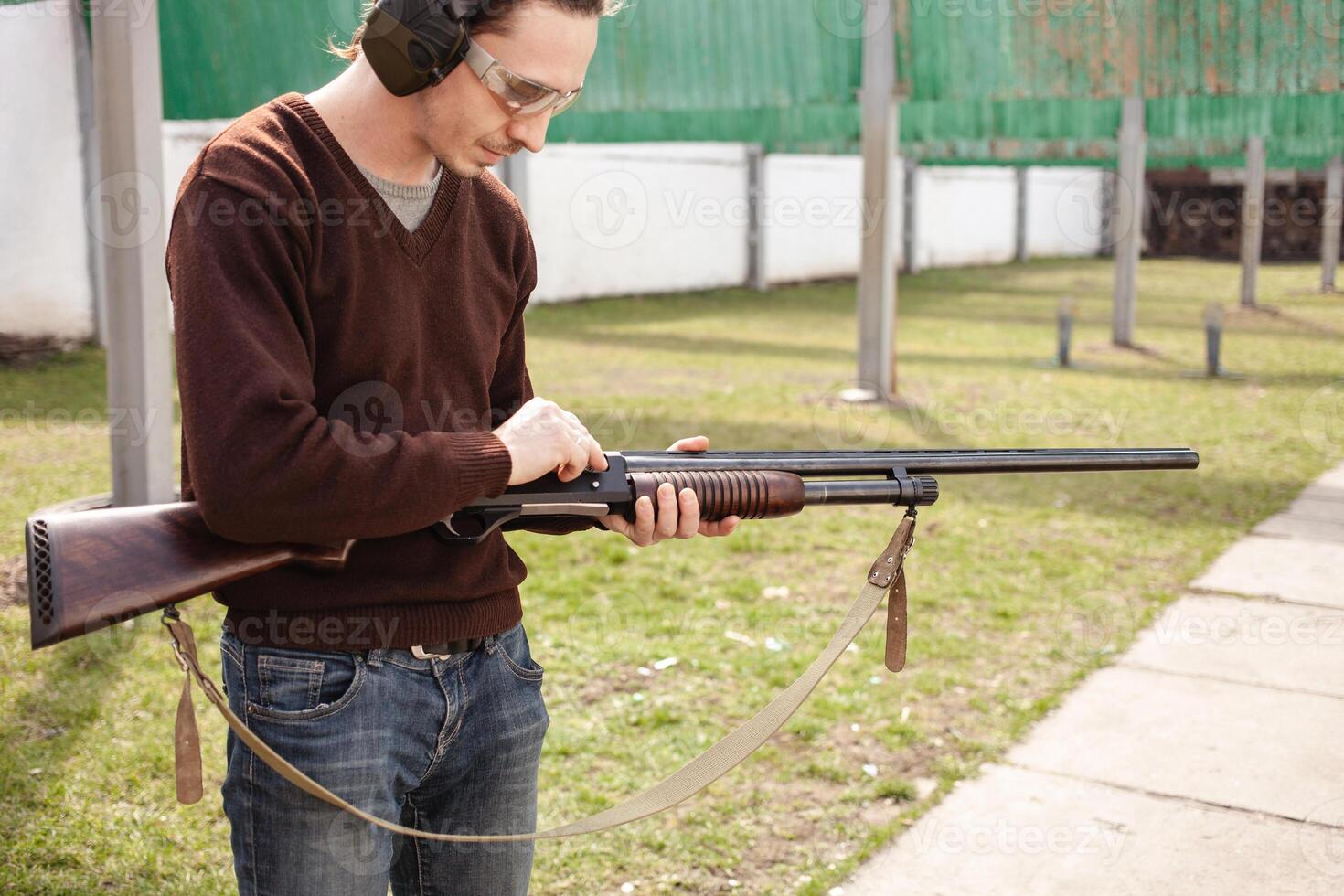 uma homem cobranças uma ação de bomba espingarda com uma munição. 12 calibre. pneu ar livre. uma homem dentro fones de ouvido e óculos é preparando para atirar. armas de fogo para Esportes tiroteio, passatempo. foto